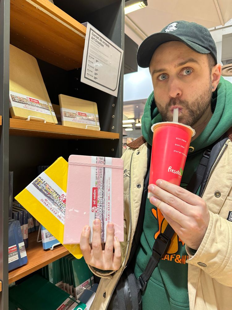 Yowan holding two notebooks (one yellow and one pink) while drinking a bubble tea