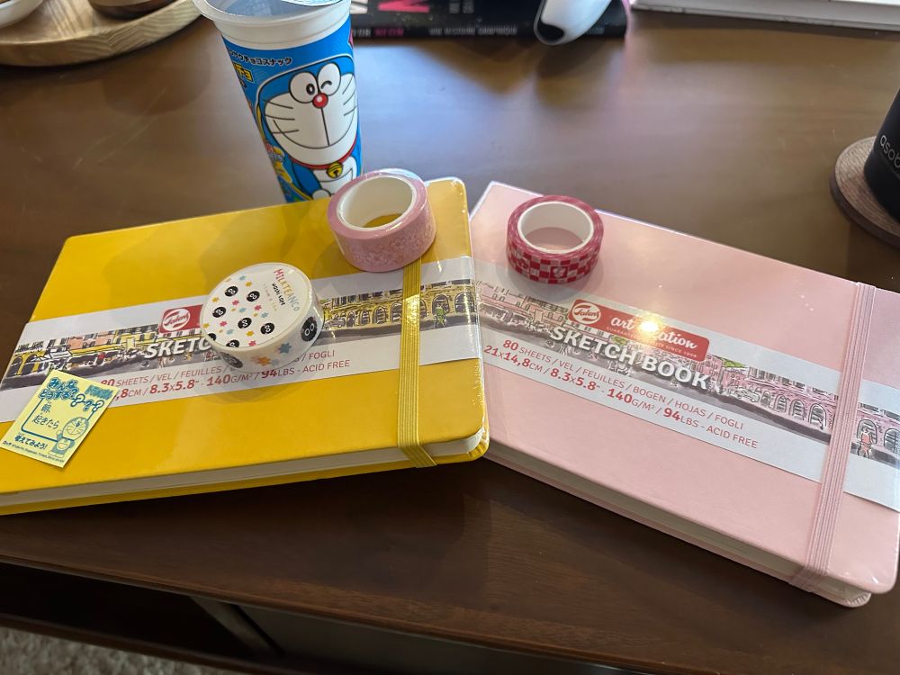 A yellow notebook and a pink notebook with a few washitapes on top