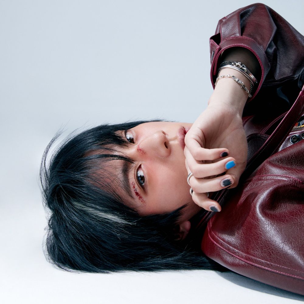 ECHO by JIN promo photo. Jin is laying on the floor looking at the camera with scars on his face and his nails painted.