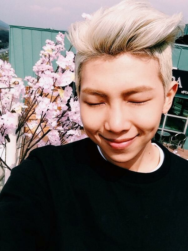 Young Namjoon with blonde hair, closing his eyes, while the sunshine radiates off of his beautiful face and the cherry blossoms behind him.