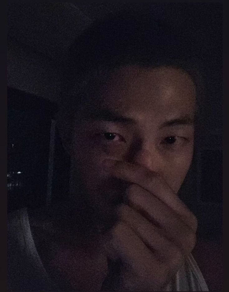 Namjoon in a dimly lit room giving a finger heart.