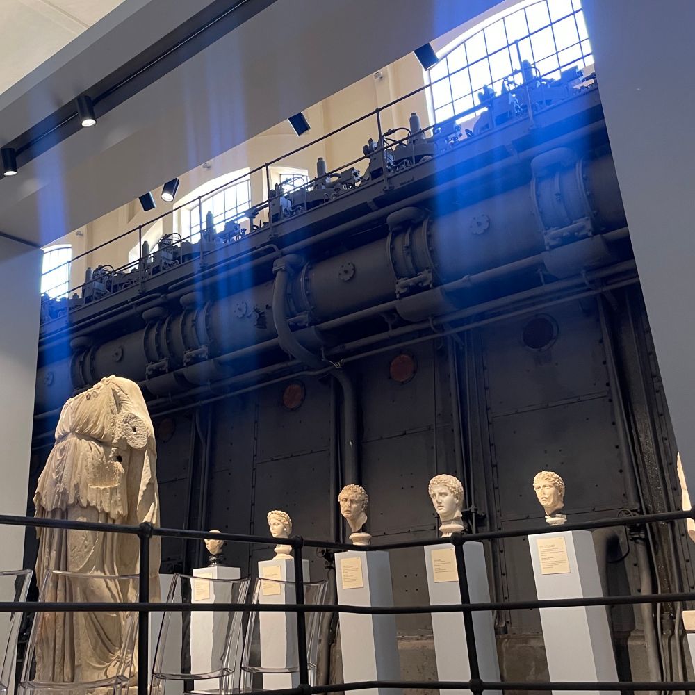 Ancient Roman busts arrayed alongside a huge black iron steam boiler with contraptions along the top that echo the rank of disembodied heads.