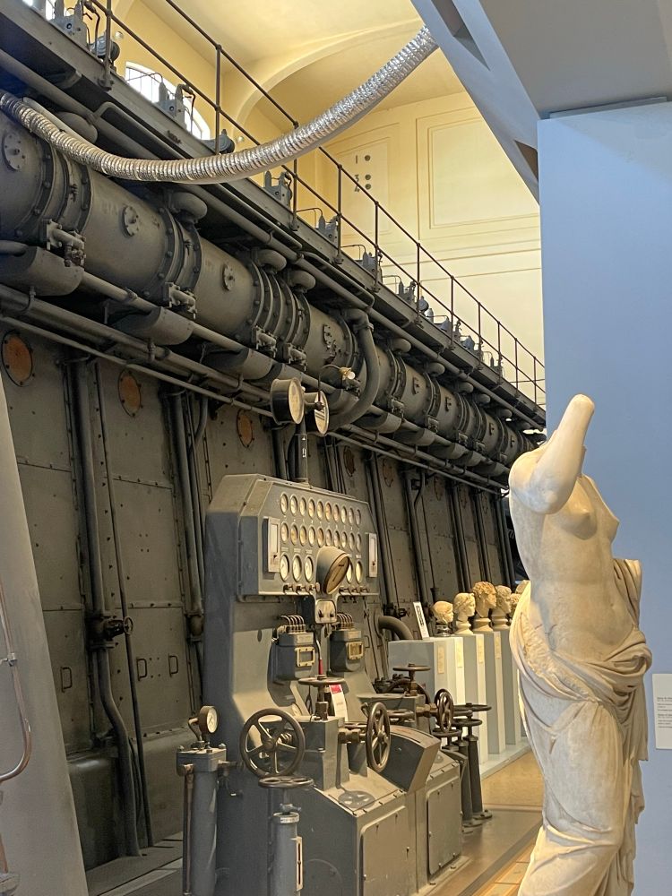Busts and a headless statue from ancient Rome beside a huge black iron boiler, as well as it's control panel.