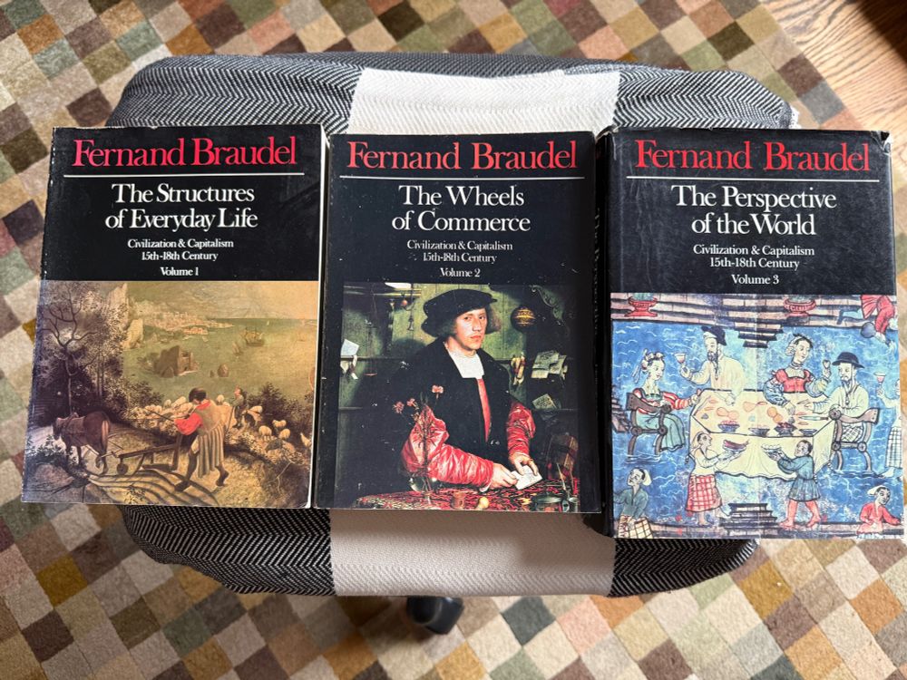 Top-down image showing the covers of Fernand Braudel's three-book series on Civilization and Capital: The Structures of Everyday Life, The Wheels of Commerce, and The Perspective of the World.