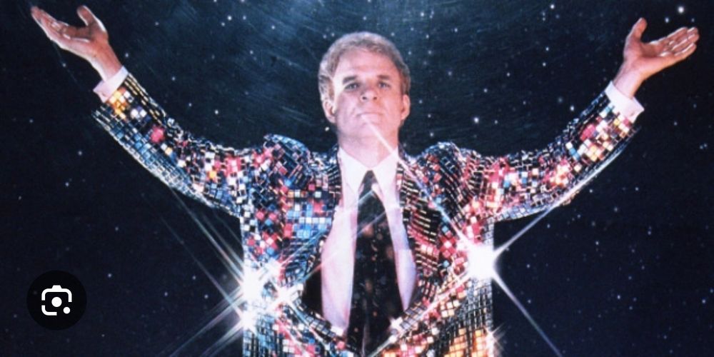 Steve Martin in Leap of Faith (movie). His arms are raised & he is wearing a sparkly silver jacket to match his silver hair. 