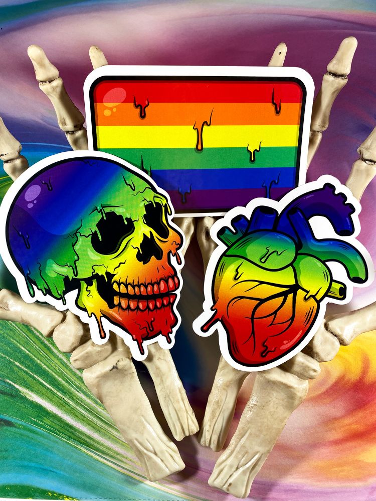 Rainbow Pride sticker skull, flag and anatomical heart. They are held in cupped skeleton hands against a colorful background.