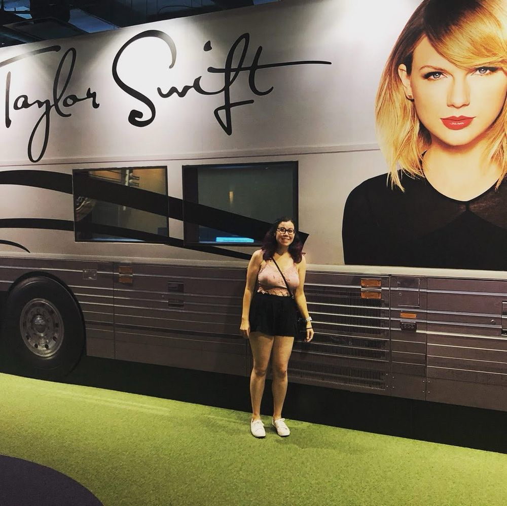 A young woman with brown hair, black shorts and a purple top standing in front of Taylor’s tour bus at the Country music hall of fame. 
