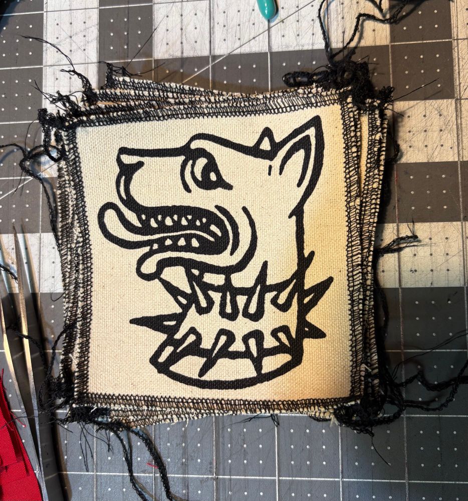 A canvas patch with a design of a medieval dog head with a spiky collar in black ink 