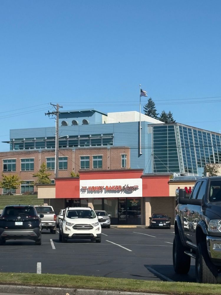 A photo from a parking lot of the Honey Baked Ham store with the Tacoma Police Dept building behind it 