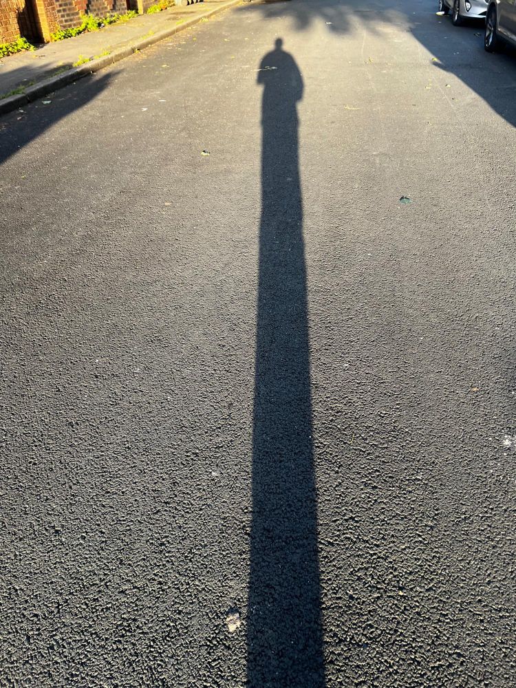 Shadow of a man on a road. It’s very long. 