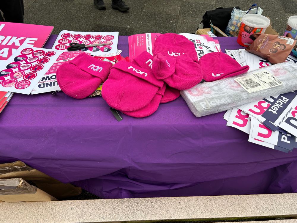 A purple trestle table with hot pink ucu bats, stickers and posters saying “on strike today”