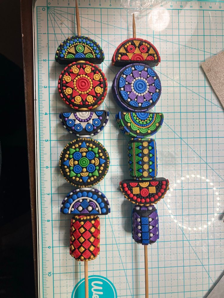 12 polymer clay items in two rows, made in three shapes, circle, half circle, and cylinder. Each item is patterned with smaller geometric shapes.