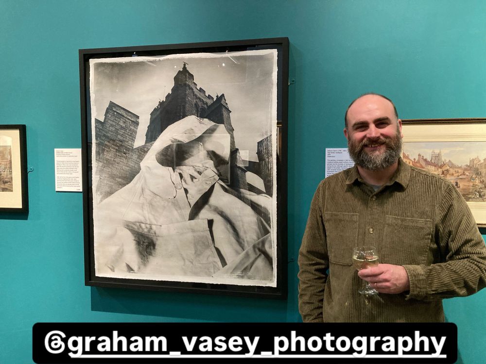 Smiling man next to large black and white art piece featuring a church and a coat 