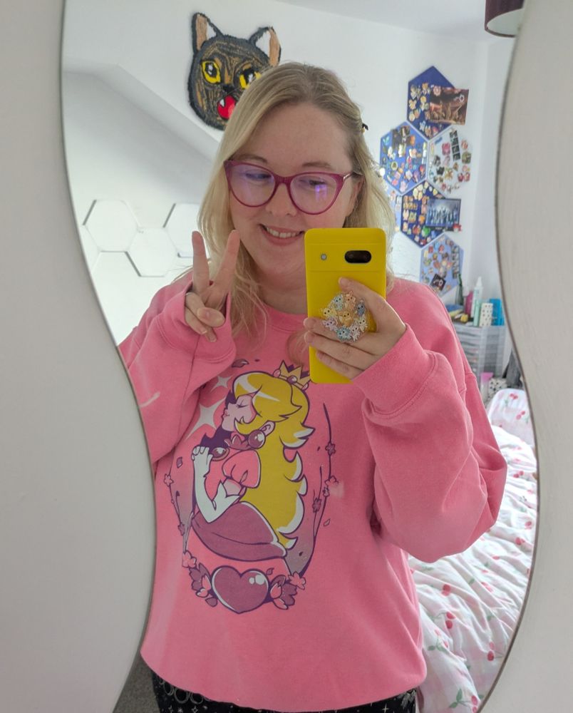 Blonde girlie wearing a pink princess peach jumper, doing a peace sign