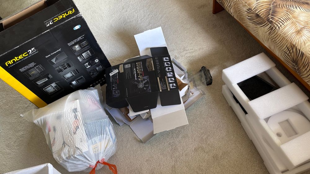 A different stack of flattened cardboard, a large computer case box to be broken down, a trash bag full of non-recyclable boxes and packing material, and a stack of packing foam.