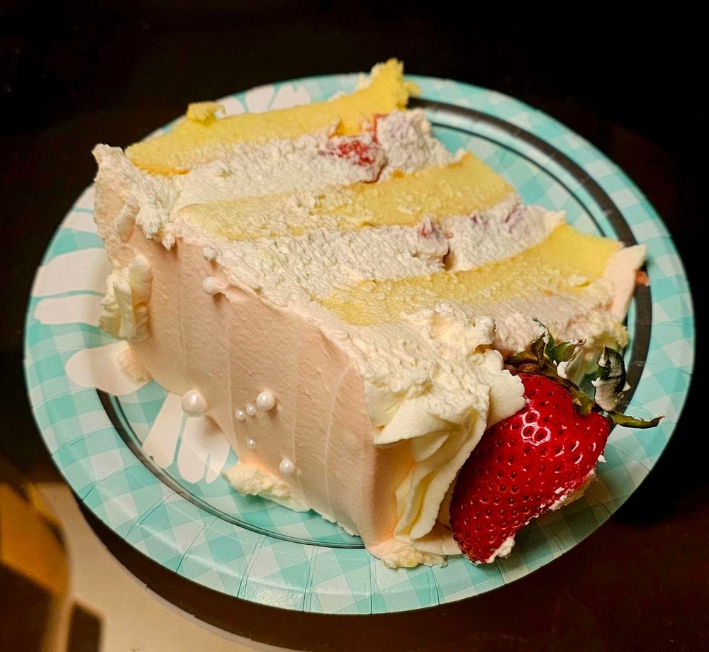 A slice of cake that has strawberry frosting, with strawberry fruit on it and inside the layers of cream.
