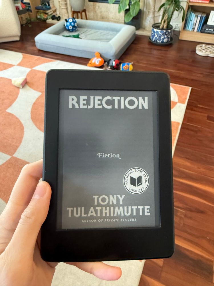 A kindle with the cover of the book Rejection by Tony Tulathimutte 