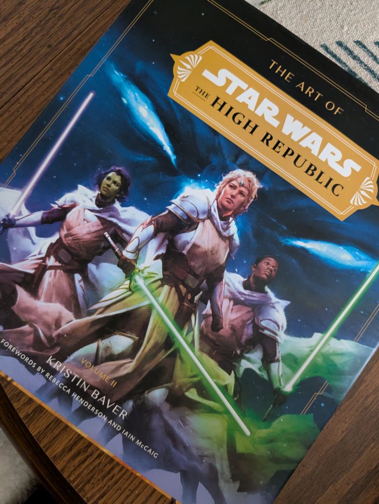 Picture of The Art of Star Wars: The High Republic Volume 2 book sitting on a table. The cover depicts three Jedi, wearing armor, as a nefarious set of eyes looms in the background