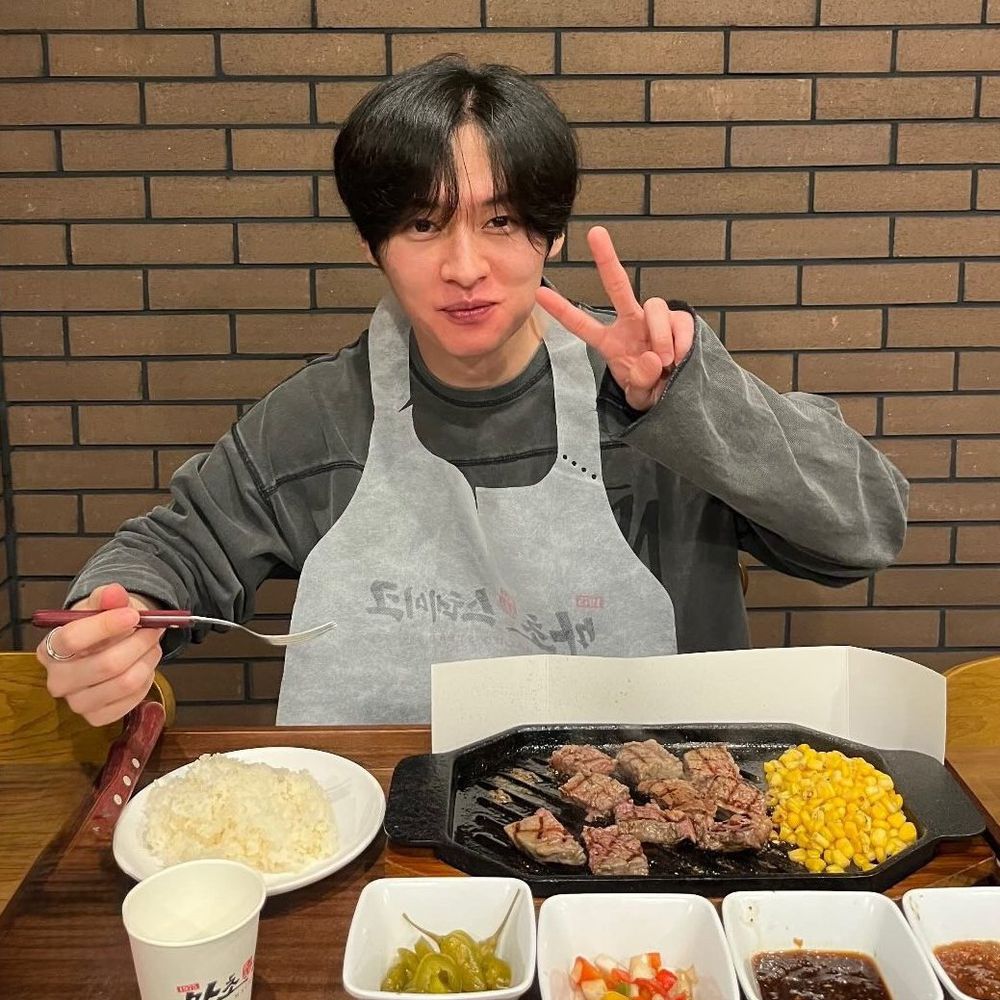 adorable precious GORGEOUS barefaced minho giving a shy smile and a V sign, sitting at a table with rice, meat, and sides all around it. 