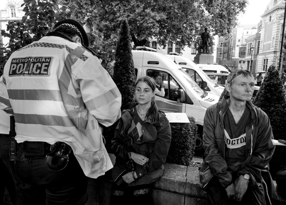 Two people sitting on a wall in handcuffs with the back of a police officer visible to the left 