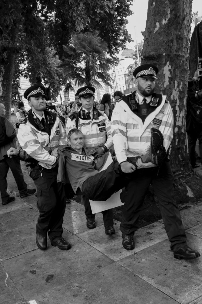 A man being carried by three police officers in uniform