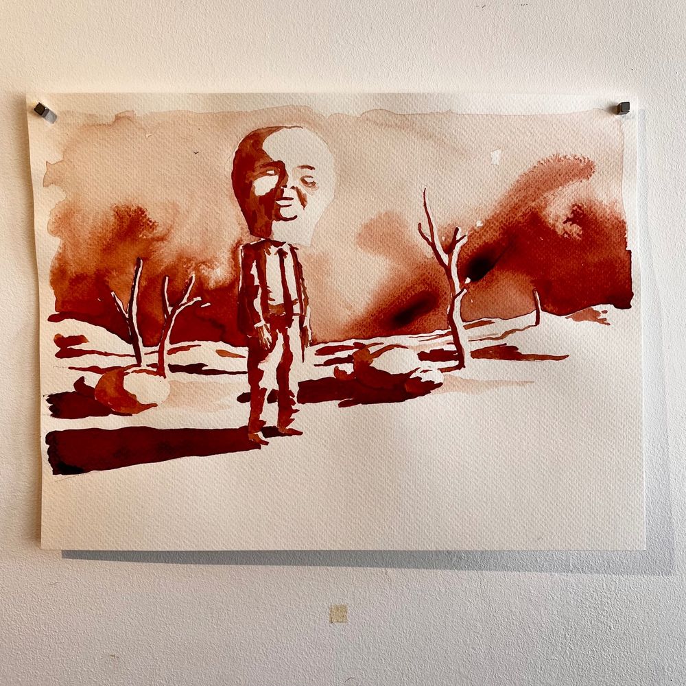 Another drawing with red ink : a man stands in a sort of desert with some tree limbs and rocks, the light is violent. He seems helpless, in a suit with another oversized mask. The sky is red and half dark.