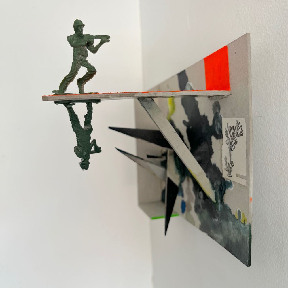 A small wall sculpture made of cardboard, with little  pikes of cardboard, and splashes of dark ink. Two plastic toy soldiers are kind of reflecting themselves on a reflex orange plank. A little picture of some algae is glued.