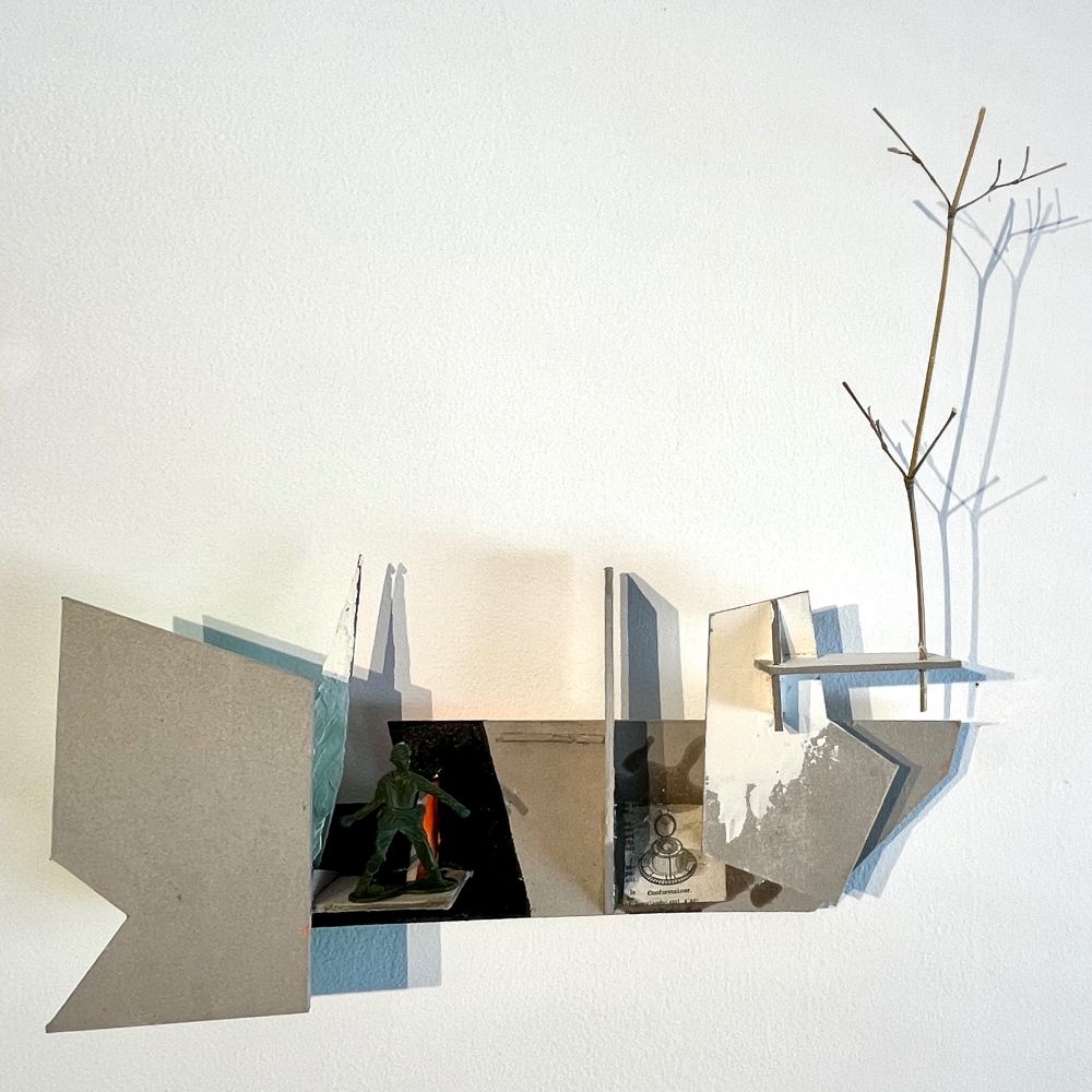 A small wall sculpture made of cardboard, with different levels of different shapes. Some are covered with plaster, some are covered with dark ink, one is reflex orange. On one of the parts there is a cheap toy soldier throwing something. an engraving with some old strange tool is glued, the legend says it’s a conformateur. On one of the shelves, a piece of bamboo evokes a dead tree. The overall size is 25×25 cm.
