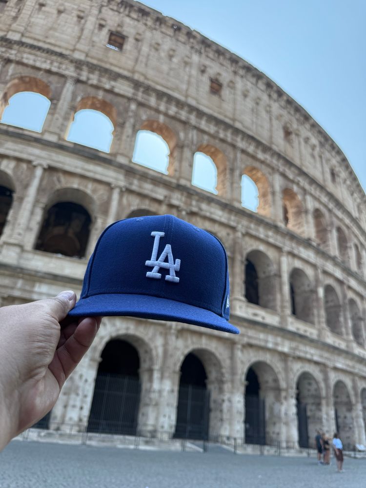 Dodger hat being held aloft in front of the colosseum in Rome