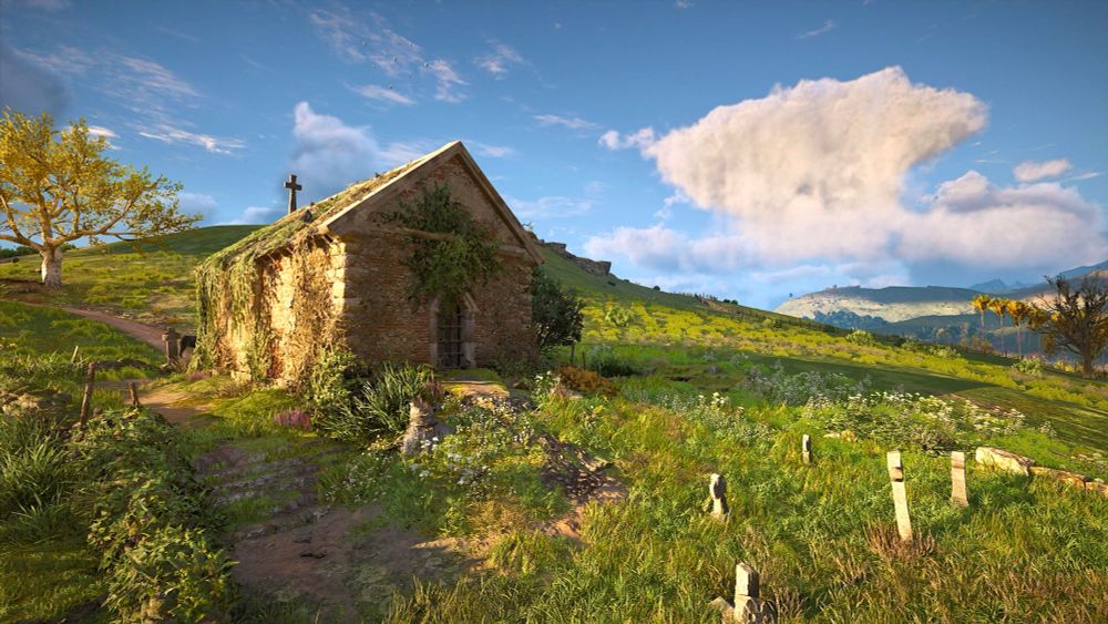 A small medieval church on a lush green hill in the English countryside. A handful of tombstones can be seen in front of the church.