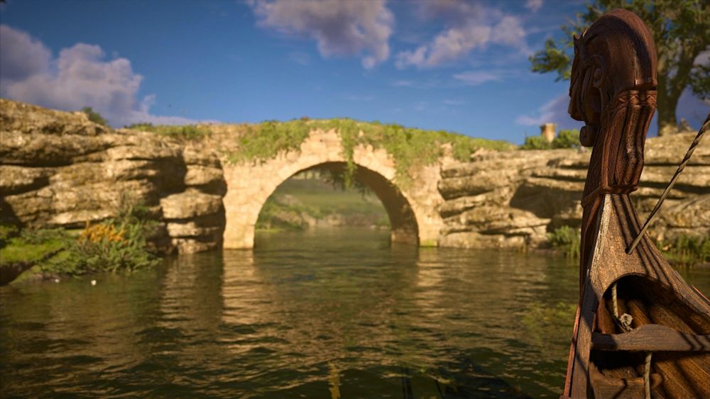 The helm of a small Viking boat is seen in the foreground with a small stone bridge in the background.