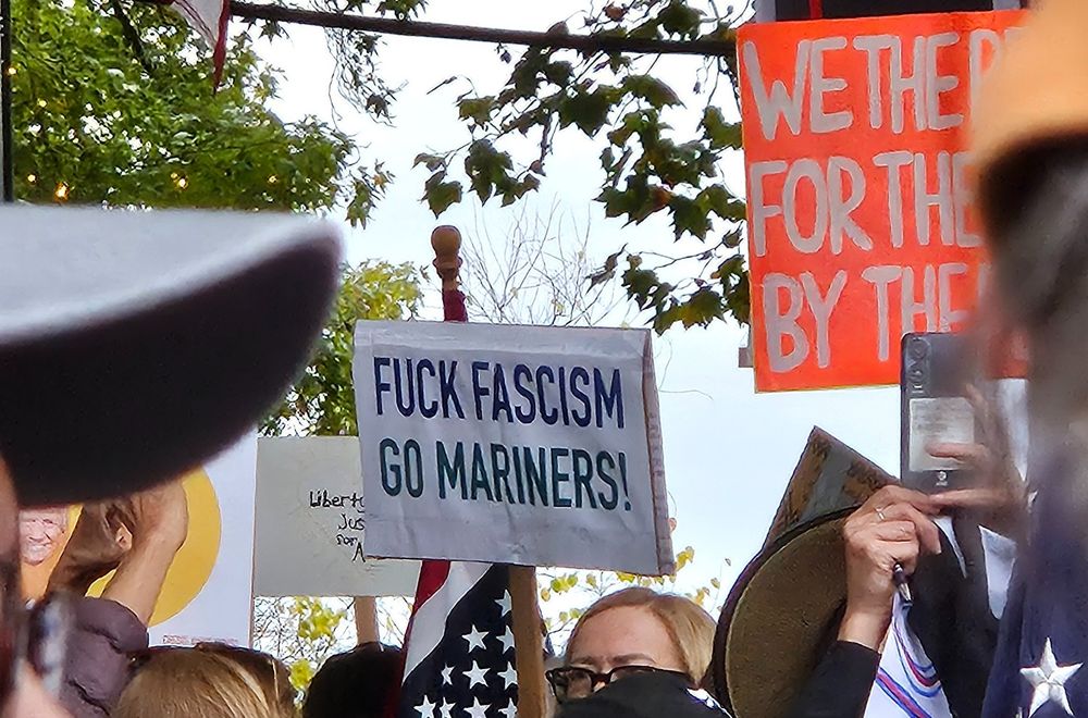 Someone at the Seattle No Kings protest holding a sign that says "FUCK FASCISM GO MARINERS"