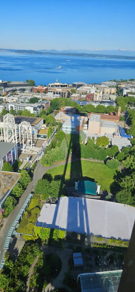 Long shadow of the Space Needle cast over Seattle Center with Elliott Bay in the background