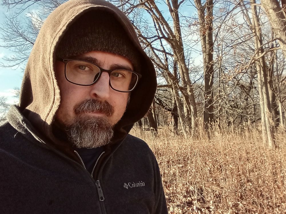 A cold Jesse stands in front of February trees and prairie.