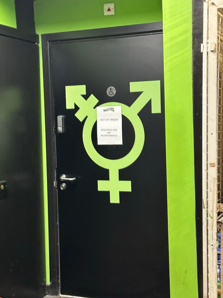 Door to a disabled toilet with a gigantic like green transgender symbol on it, over which is stuck a sheet of A4 paper announcing:
AFFLECK’S
OUT OF ORDER
APOLOGIES FOR ANY INCONVENIENCE
and then the door also has a key code lock on it.