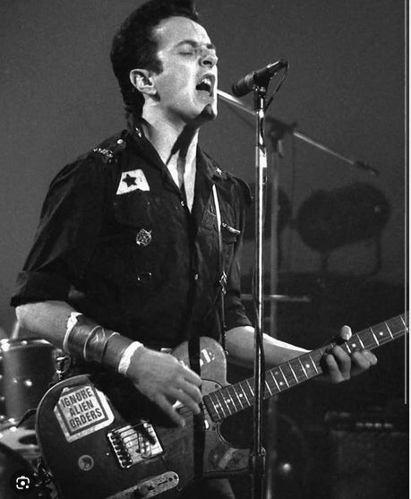 Joe Stummer of The Clash onstage with "Ignore Alien Orders" sticker prominent on his guitar