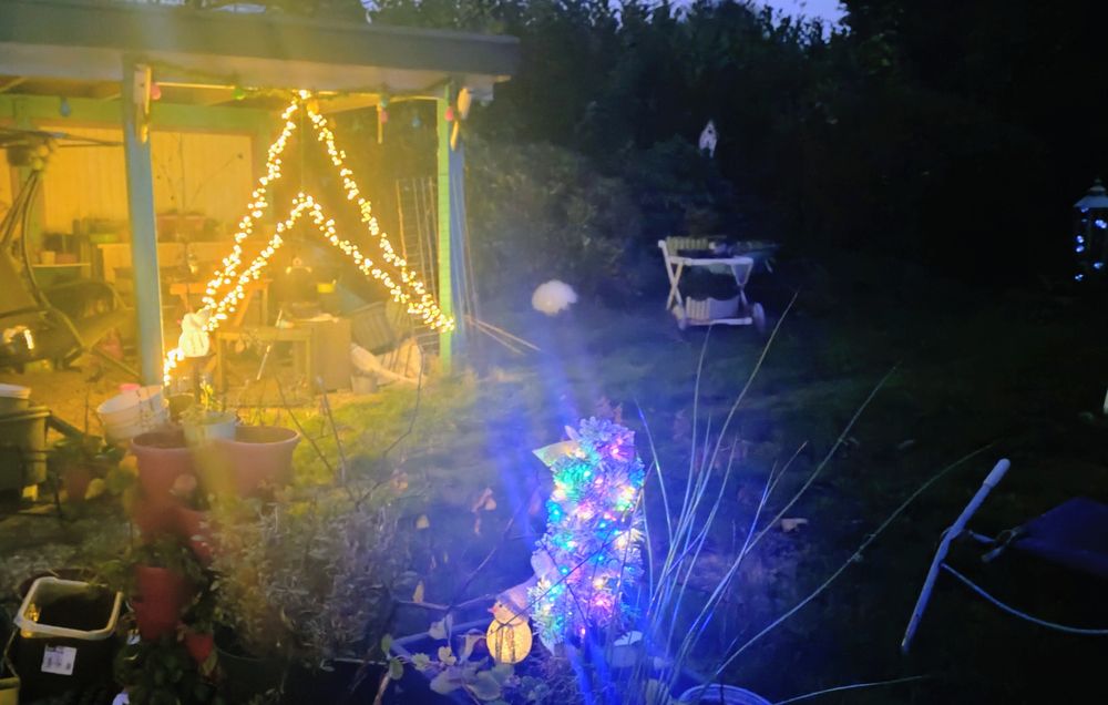 Eine Lichterkette in Form eines doppelten dreicecks zwischen den carportfposten und im Vordergrund ein kleiner beleuchteter weihnachtsbaum. Mit kleinem Schneemann davor. 
