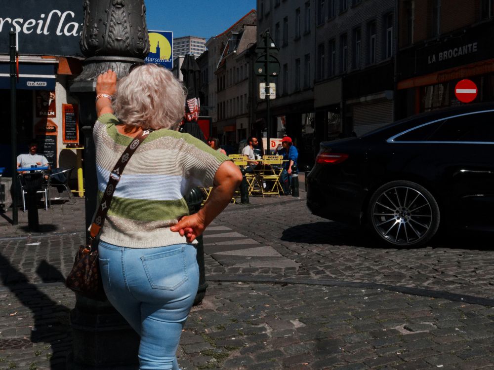 Middle-aged woman in Brussels, photographed from behind, on a street corner. 