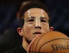 Phoenix Suns player Devin Booker wearing a clear facial protective mask while holding a basketball. 