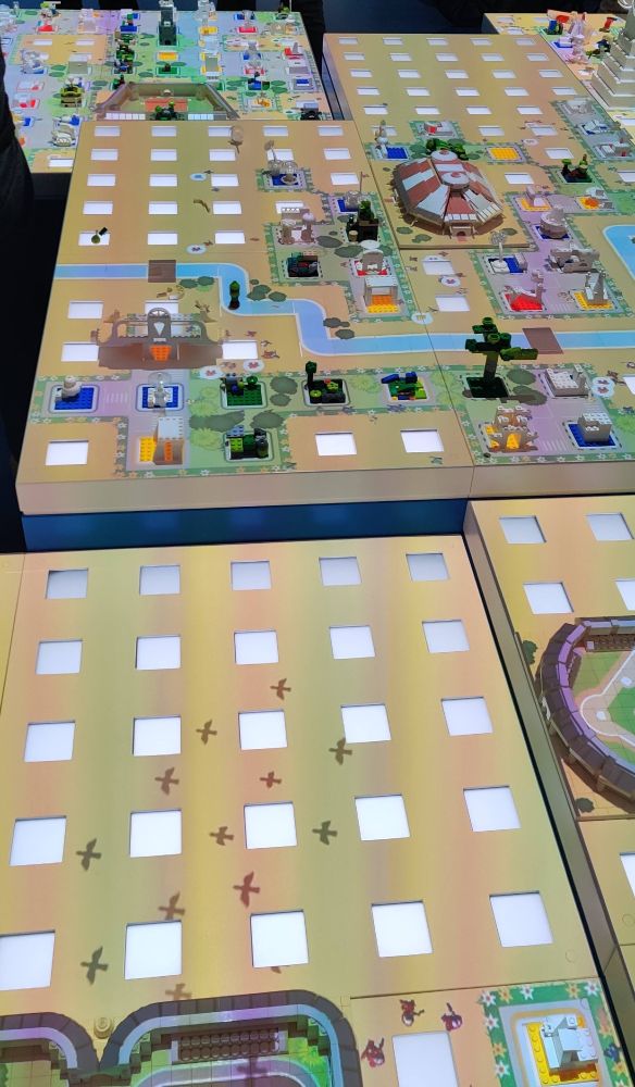 The Lego city building area in Lego House, Billund. A table has a grid pattern where Lego plates can slot in. The plates can have any kind of building on it you can image; the color of the base plate is picked up by a camera and it projects the surrounding greenery, roads and animated people.