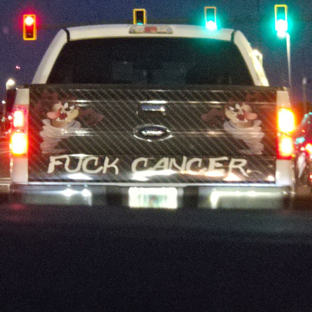 picape com um adesivo grande na traseira com um Taz de cada lado e a frase fuck cancer 