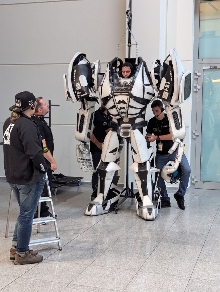 A cosplayer is helped into a mecha costume
