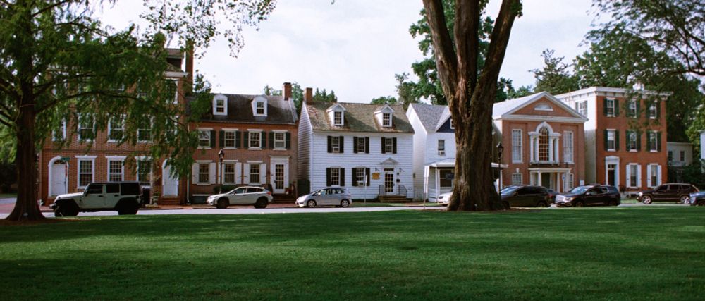 A color film photograph of the Dover Green at the Old Statehouse in Dover, DE. "The Dover Green was laid out in 1717, following a plan created by William Penn in 1683, to serve as a gathering area for the growing town. The Green has played a role in the American Revolution, founding of the nation, Women’s Rights, Civil Rights and more."
