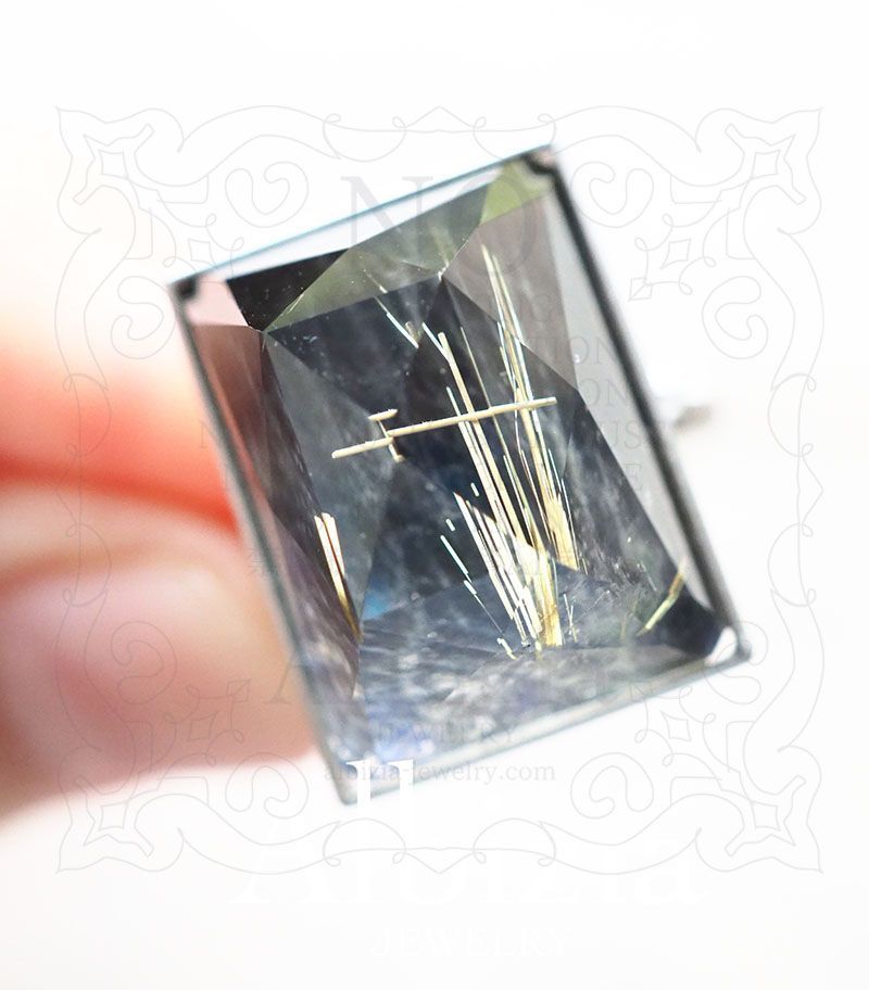 スペクトロライトとルチルクォーツのダブレットストーンのリング。長方形のミックスカット。覆輪留め。地金はPt900。リングを手に持って上向きにして撮った写真です。