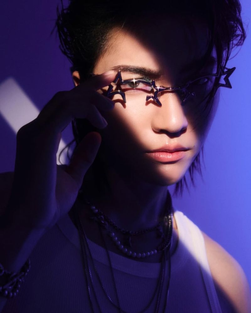 divesth @ instagram | Close-up photo of Boss with deep purple lighting over the background and all but a stripe of regular light diagonal across his face and shoulder the width of one eye. He's wearing silver Gentle Monster glasses with stars at the outer edges of the frames, silver chain necklaces, and a white tank top that also appears purple in the light. He's looking straight into the camera with a neutral expression, one hand up with a finger to his glasses, and there is pink and green eyeshadow visible around his illuminated eye. There are a couple exaggerated white sparkles placed over the glasses

#bossckm