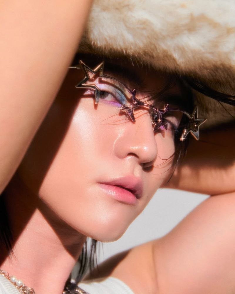 divesth @ instagram | Photo of Boss from an angle, from the shoulders up in front of a white background. He's wearing a white fur cowboy hat, silver Gentle Monster glasses with star shapes at the outside of the frames, silver chain necklaces with stars and pearls, and a white tank top. His hands are both up behind his head and he's looking into the camera with a neutral expression, blue, pink, and purple eyeshadow visible around his eyes

#bossckm