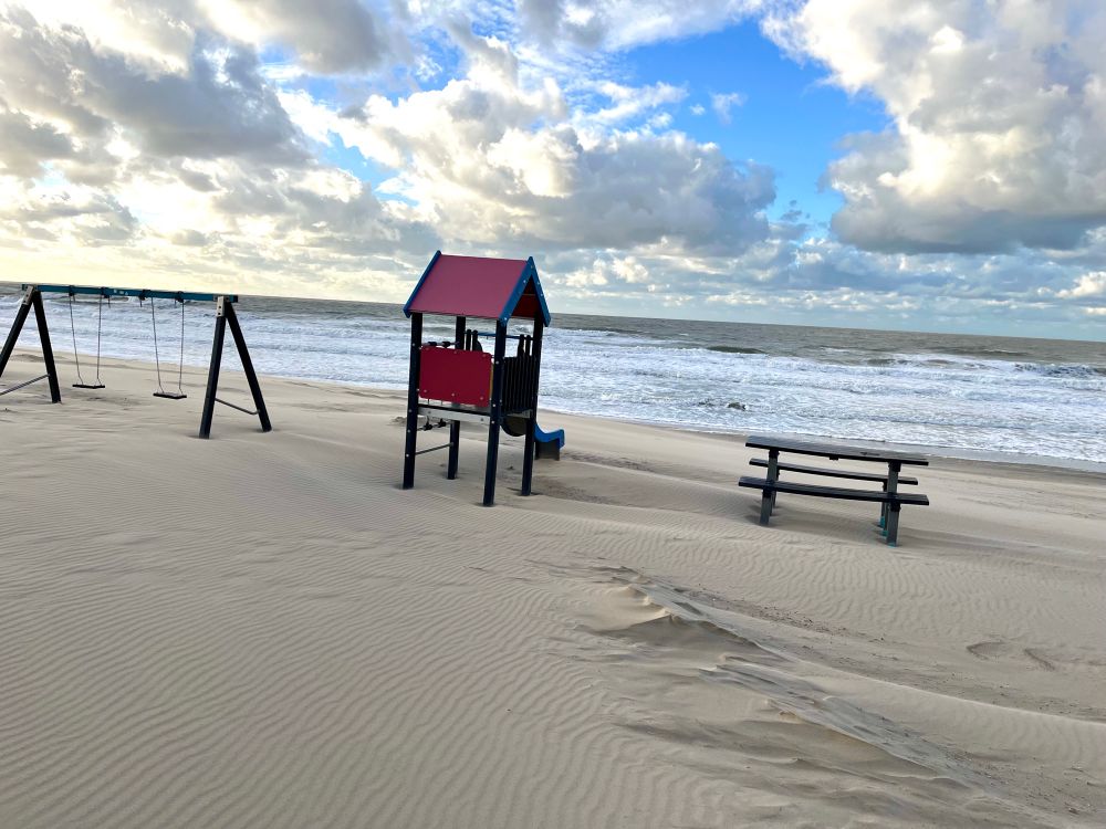 Mini playground on a beach. Swings and a slide looking at the sea.