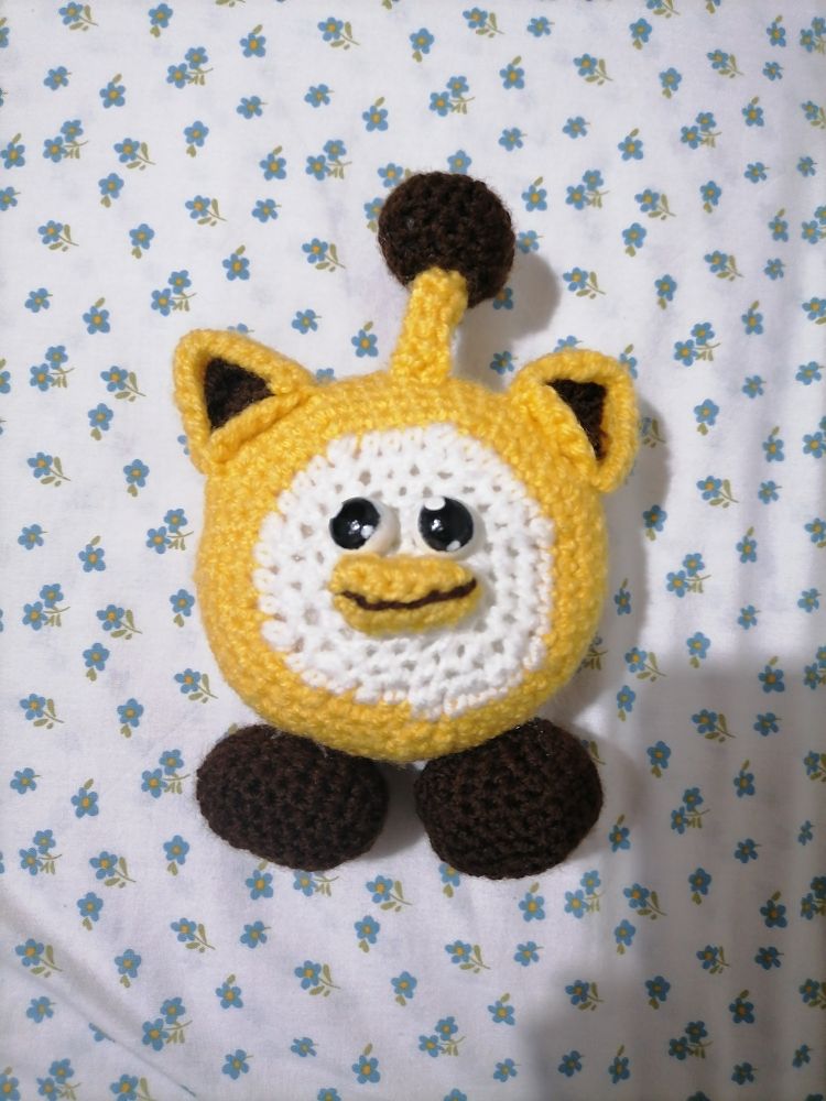 Photograph of a crocheted doll of a Ouioui, a fictional character from the company Itemlabel, that resembles a ball with a beak, cat ears, an antenna and two little feet. 
