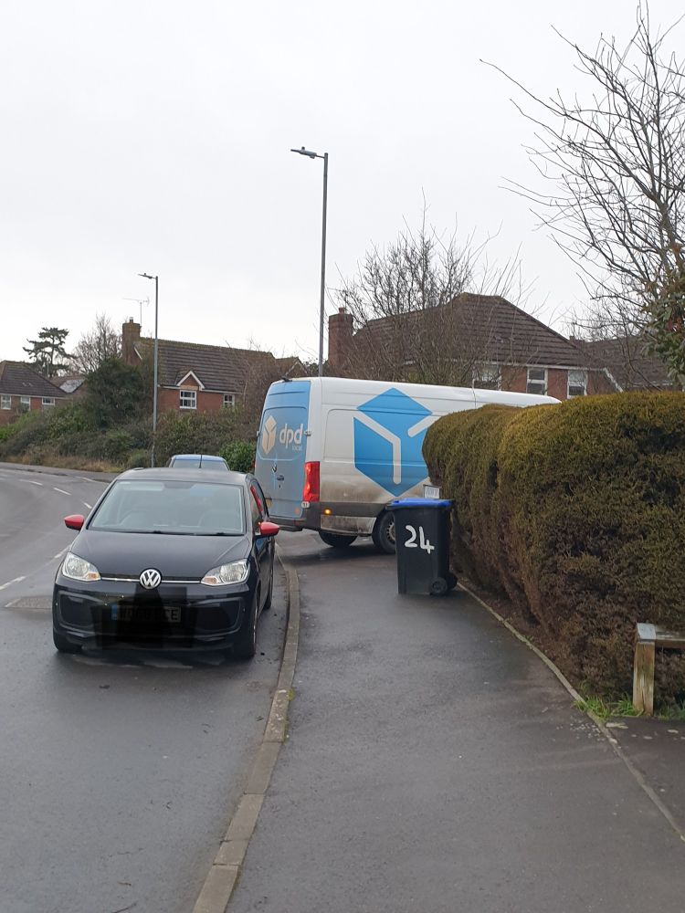 A delivery van blocking a pavement. It is parked between two cars who are on the road.