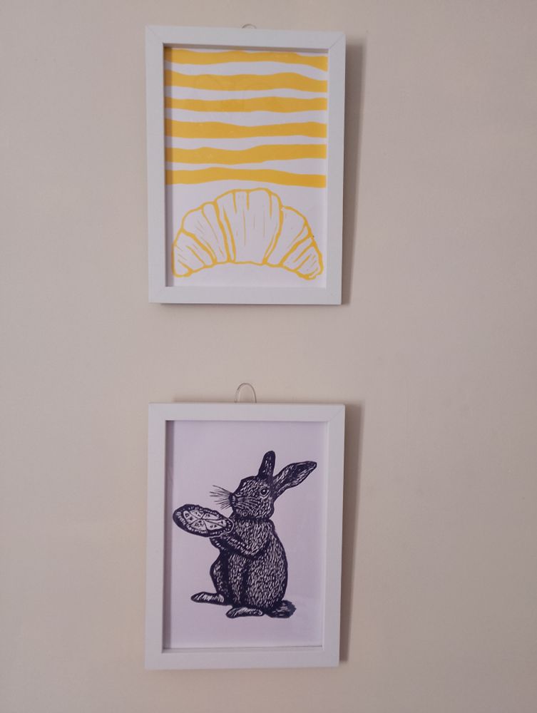 Two more lino prints from @sundownerstudio.bsky.social
Top to bottom: a yellow croissant below yellow wavy lines. A dark blue rabbit holding a pizza, the rabbit looks pleased to be holding the pizza and showing it to you
Both prints set in white frames 